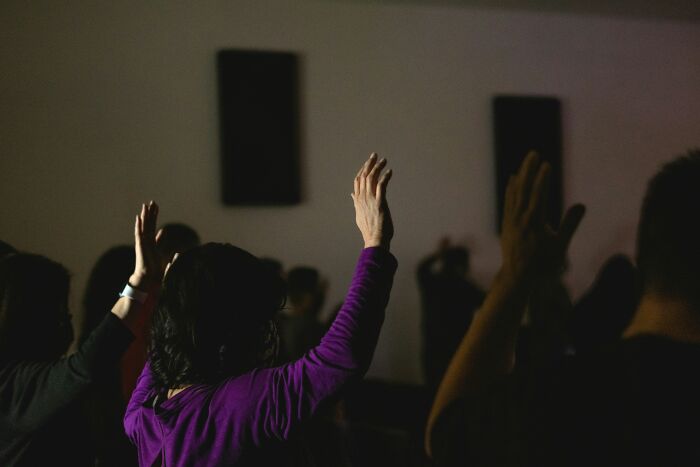 Audience members raising their hands in a dark room, highlighting performative behaviors in social settings and society.