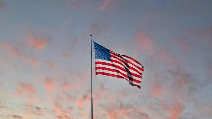 American flag waving on a flagpole at sunset, illustrating aspects of modern life frighteningly close to breaking down.