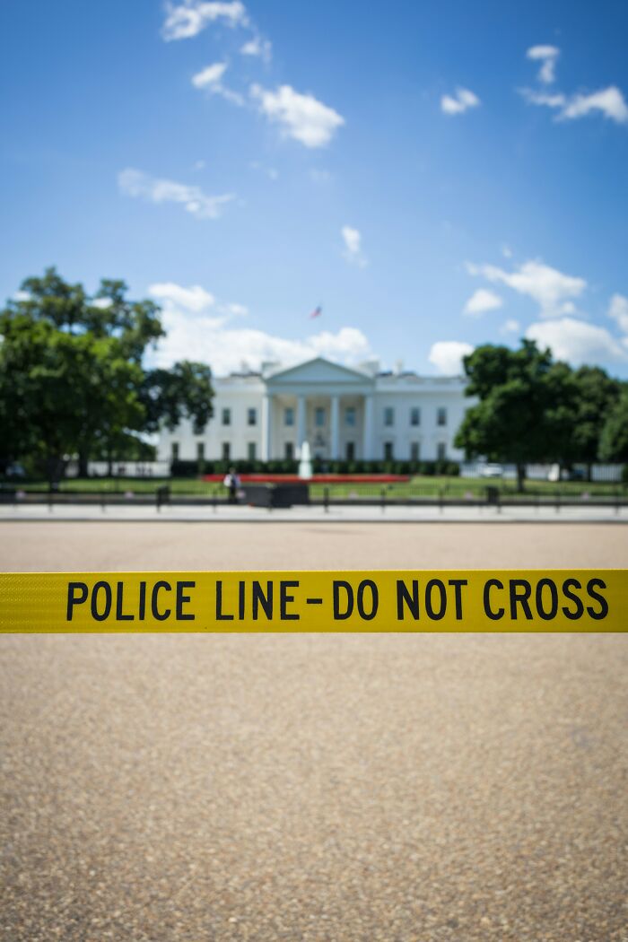 Yellow police line tape with do not cross text in front of the White House under a blue sky, illustrating disturbing facts.