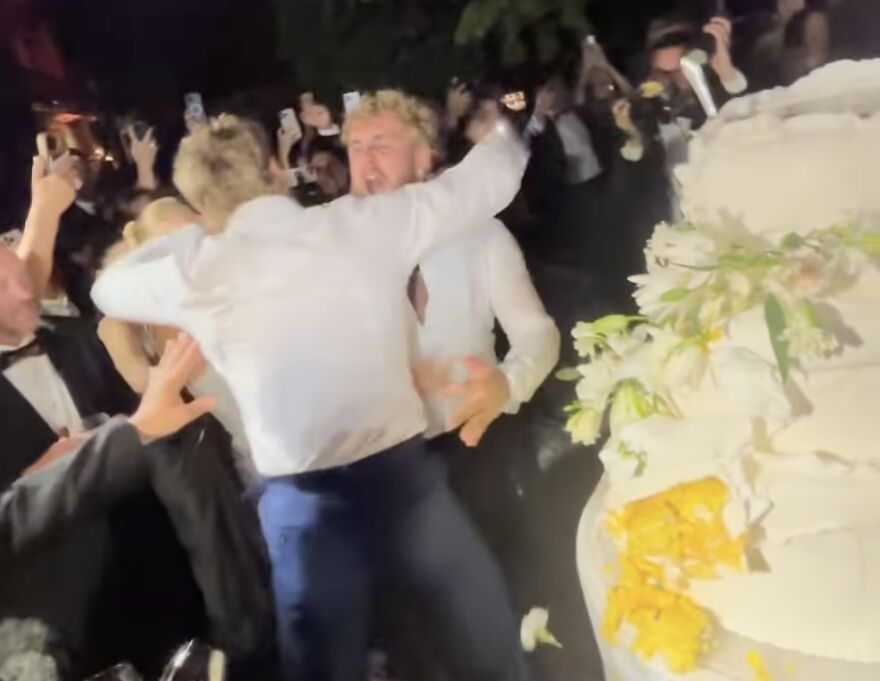 Jake Paul smashing wedding cake at Logan Paul's wedding, surrounded by guests capturing the bizarre viral moment.
