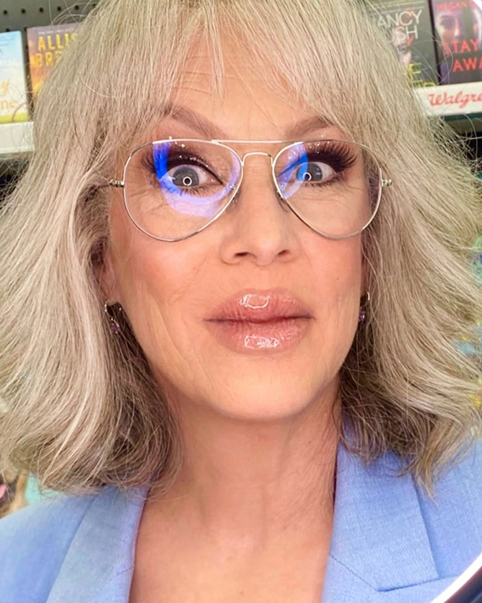 Jamie Lee Curtis with dramatically fuller lips, wearing clear glasses and a blue blazer, posing indoors. Jamie Lee Curtis with dramatically fuller lips, wearing clear glasses and a blue blazer, posing indoors.