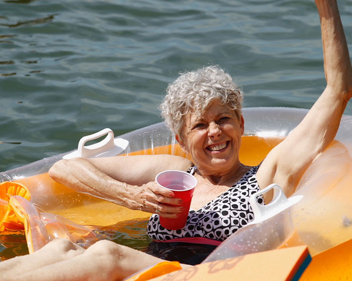Smiling elderly woman relaxing on an inflatable float in water, holding a red cup, symbolizing Brad Pitt's final public message to his mom. Smiling elderly woman relaxing on an inflatable float in water, holding a red cup, symbolizing Brad Pitt's final public message to his mom.