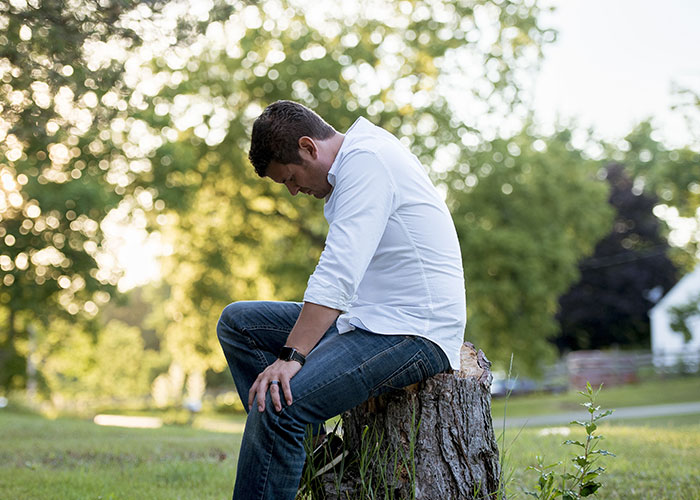 Man in a white shirt sitting on a tree stump looking upset, illustrating consequences of cutting down neighbor’s trees. Man in a white shirt sitting on a tree stump looking upset, illustrating consequences of cutting down neighbor’s trees.