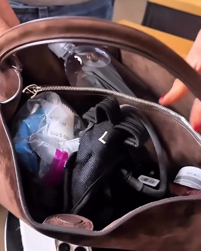 Inside of a brown purse showing everyday items including a water bottle and black gloves in Jennifer Aniston’s accidental purse reveal. Inside of a brown purse showing everyday items including a water bottle and black gloves in Jennifer Aniston’s accidental purse reveal.