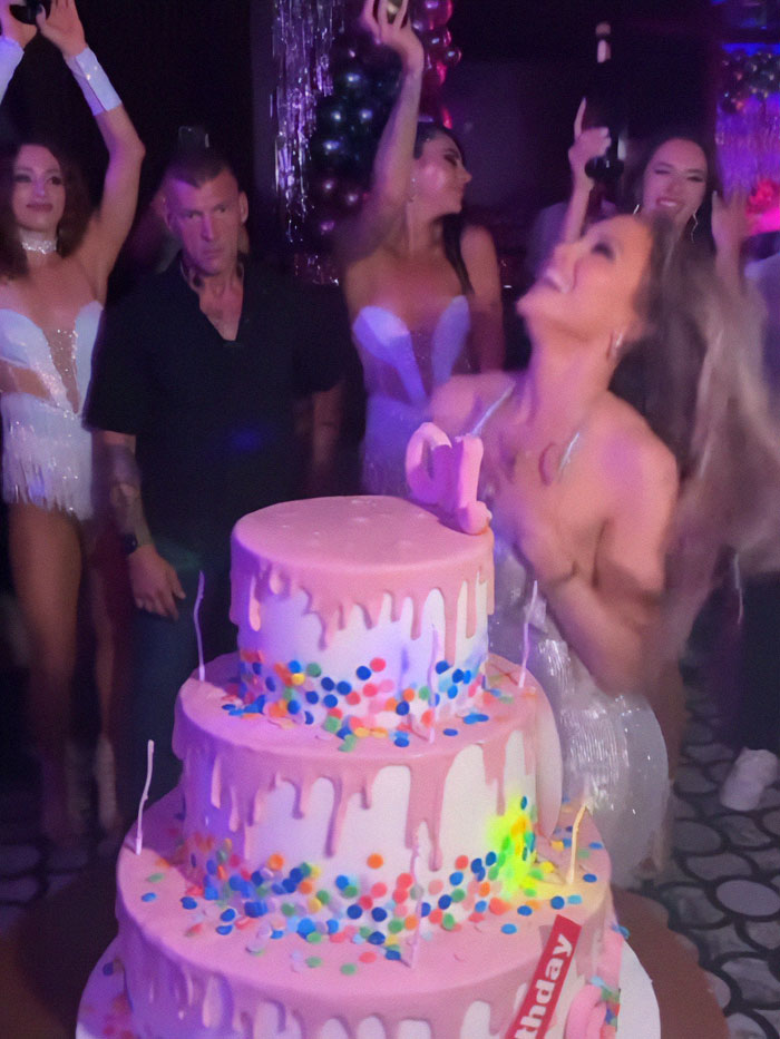Jennifer Lopez celebrating with a pink dripping cake and friends, capturing a lively party atmosphere.