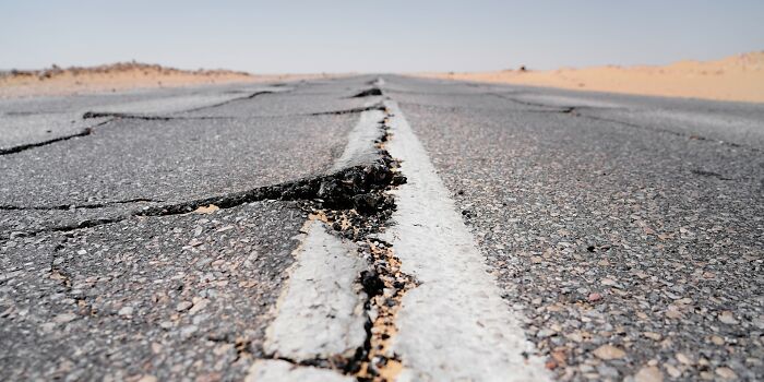 Close-up of c*****d and damaged road stretching through a desert landscape, illustrating people surviving crazy situations.