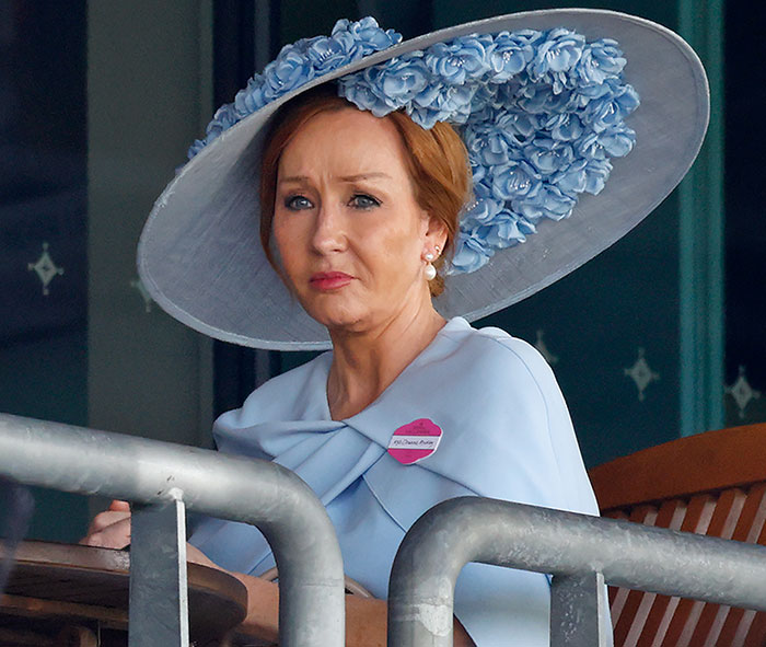 J.K. Rowling wearing a large blue floral hat and light blue outfit at an outdoor event, speaking out on controversy.