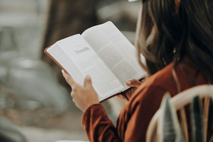 Person reading a book titled Proverbs, symbolizing hope and good news deserving the spotlight in a calm setting.