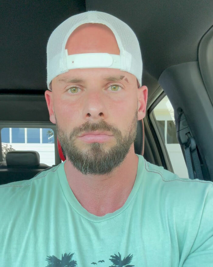 Joey Swoll wearing a white cap and green shirt, sitting in a car, reacting to critics of men under 5&rsquo;10&rdquo; height.