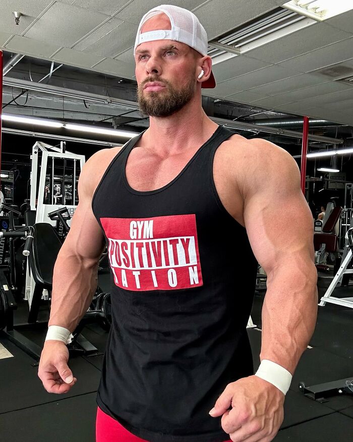 Muscular man Joey Swoll in a gym wearing a tank top with Gym Positivity Nation, looking determined and confident.