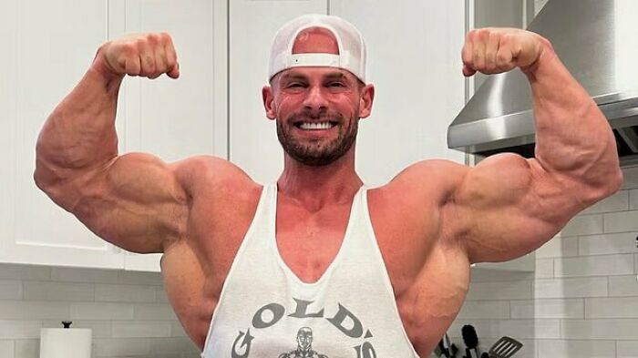 Joey Swoll flexing muscles in a kitchen, showing strength and confidence amid a social media controversy.