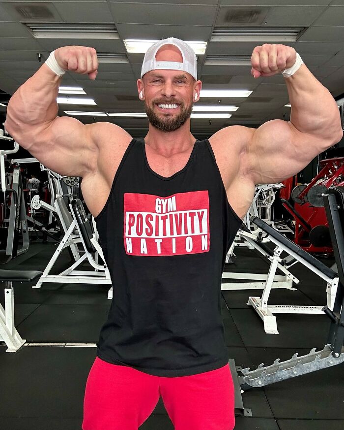 Joey Swoll flexing muscles in gym wearing Gym Positivity Nation tank top, showcasing strength and confidence.