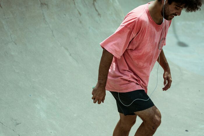 Young man wearing a pink shirt and black shorts skating in a concrete park, highlighting gender-based double standards in action.