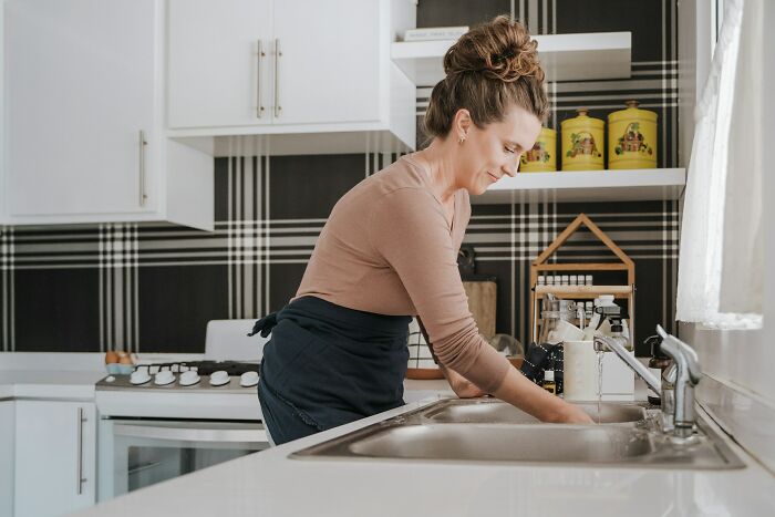 Woman washing dishes in a modern kitchen, illustrating people sharing the weirdest things seen in someone else’s home. - 13