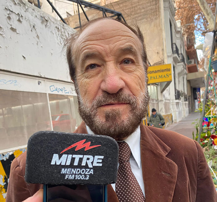 Man in brown suit and tie speaking to a Mitre Mendoza FM 100.3 microphone about celebrity duck legal support.