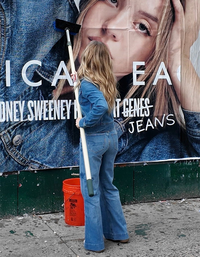 Woman in denim jeans and jacket cleaning a large American Eagle jeans advertisement on a city sidewalk.
