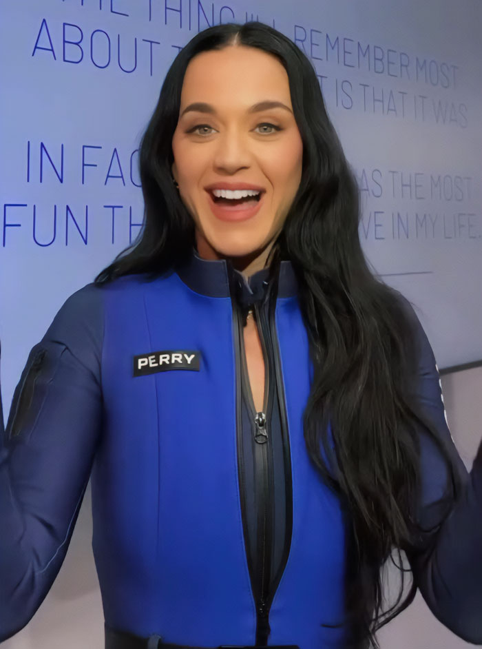 Katy Perry smiling in a blue wetsuit with her name patch visible, showcasing her style and confidence.