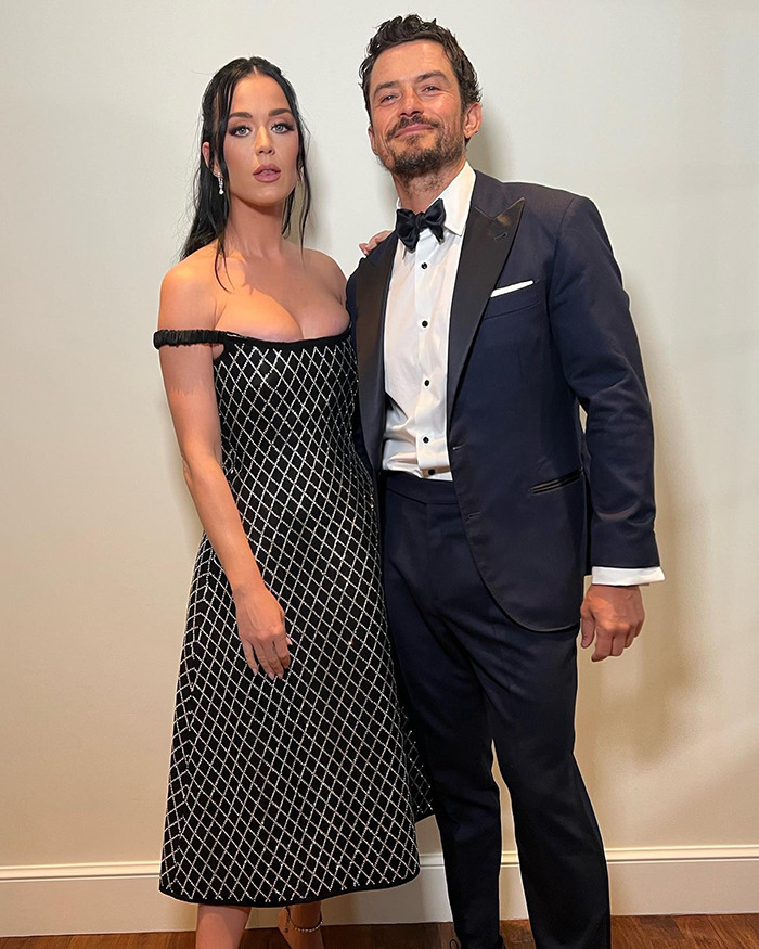 Orlando Bloom in tuxedo and Katy Perry in black dress posing together, referencing Orlando Bloom dating rumors.