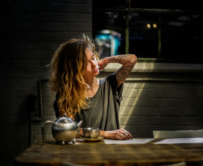 Young woman with tattoos sitting at a table with tea, reflecting on ways to avoid babysitting shared online.