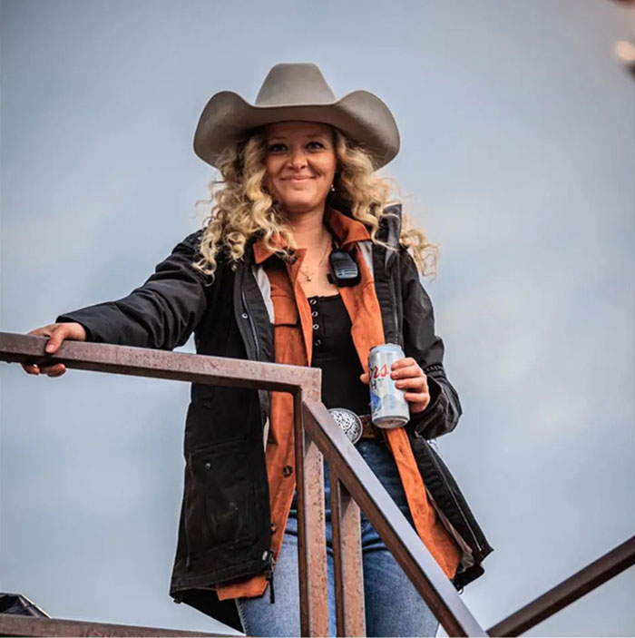 A woman with curly hair and a cowboy hat holding a can, related to Kelly Clarkson's ex-assistant in obituary news.