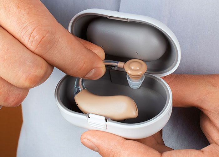 Person holding hearing aids in a charging case, relating to host kicking out friend's neurodivergent buddy incident.