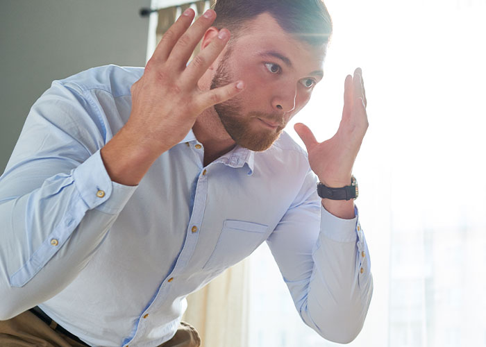 Frustrated man wearing a light blue shirt gesturing with hands, depicting tension about hearing aids and neurodivergent interaction.