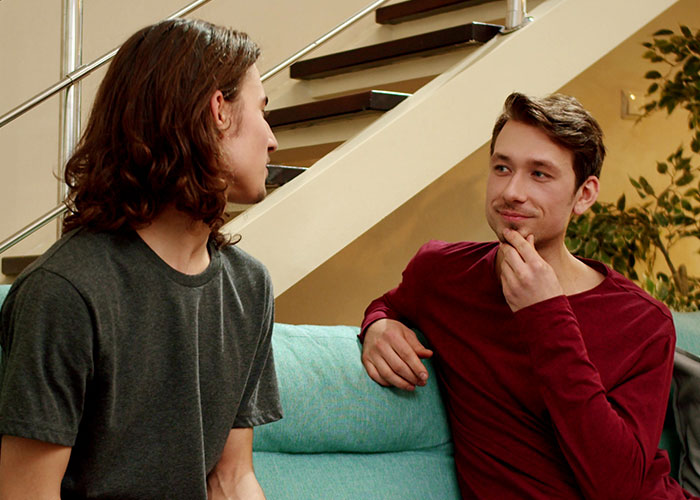 Two young men having a serious conversation on a couch, highlighting a host and neurodivergent friend situation.