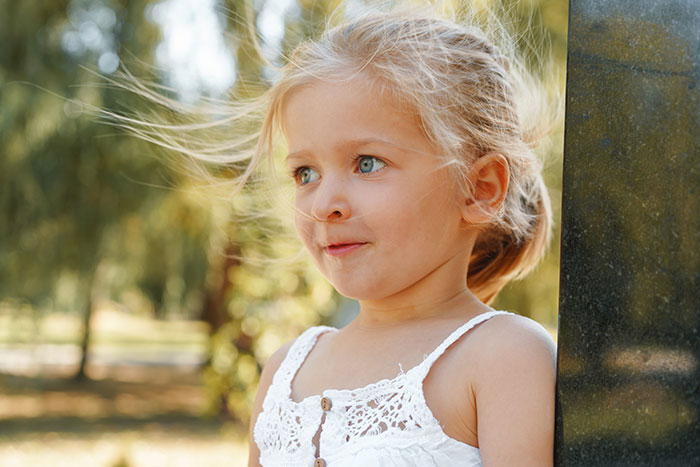 Young girl with blonde hair outdoors looking thoughtful in a sunlit park, symbolizing surviving kidnapping experiences.