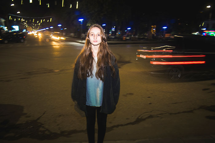 Young woman standing alone at night on a city street, evoking feelings related to kidnapping survival experiences.