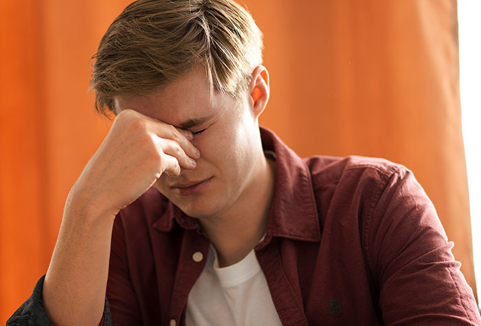 Young man in a maroon shirt holding his forehead, showing stress and fear reflecting kidnapping survival experience.
