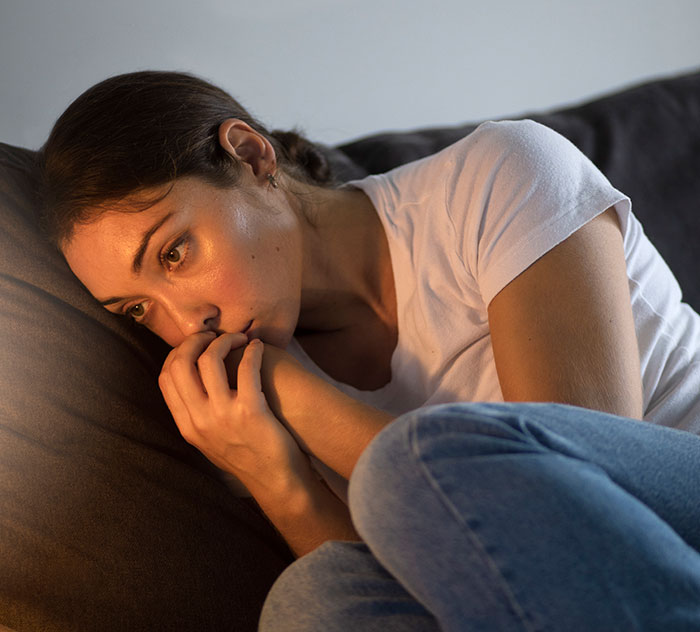 Worried woman sitting curled on couch, reflecting on horrifying kidnapping experiences and survival stories.