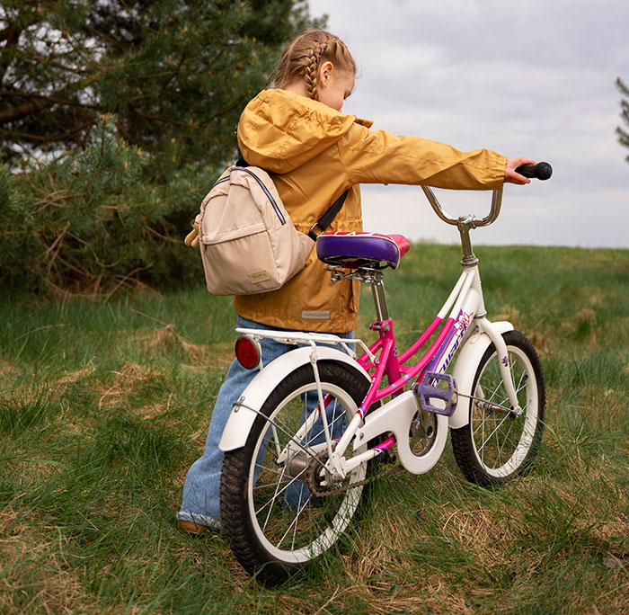 Young girl with backpack walking a bike through a grassy field, illustrating kidnapping survival experiences concept.