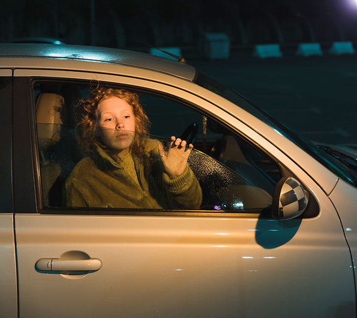 Woman inside car at night, looking distressed and pressing her hand against the window after surviving kidnapping experience