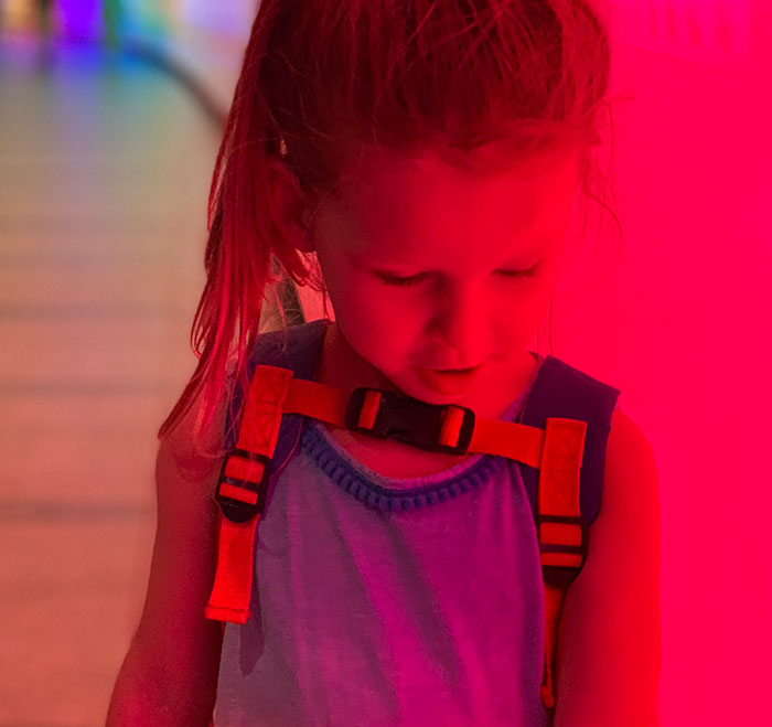 Young girl with a backpack looking down under red lighting, representing kidnapping survival experiences.