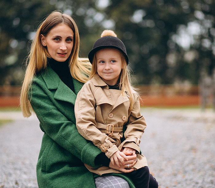 Woman in green coat holding child in beige trench coat and black hat outdoors, evoking themes of kidnapping survival experiences