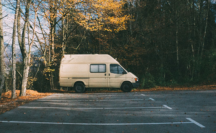 Beige van parked in an empty lot by autumn trees, evoking a scene related to kidnapping survival stories.