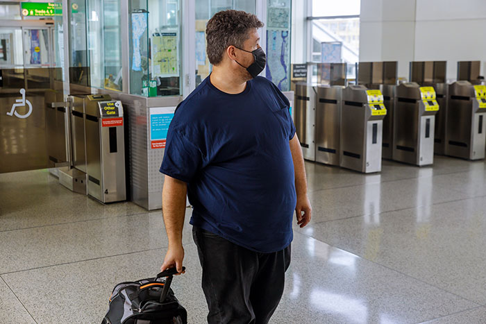 Man wearing a mask holding luggage in a transit station, illustrating embarrassing moments parents will never forget with kids.