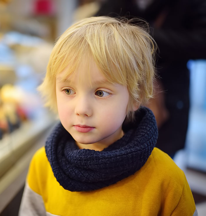 Blond child wearing a yellow shirt and dark blue scarf, looking to the side, capturing embarrassing moments parents will never forget.
