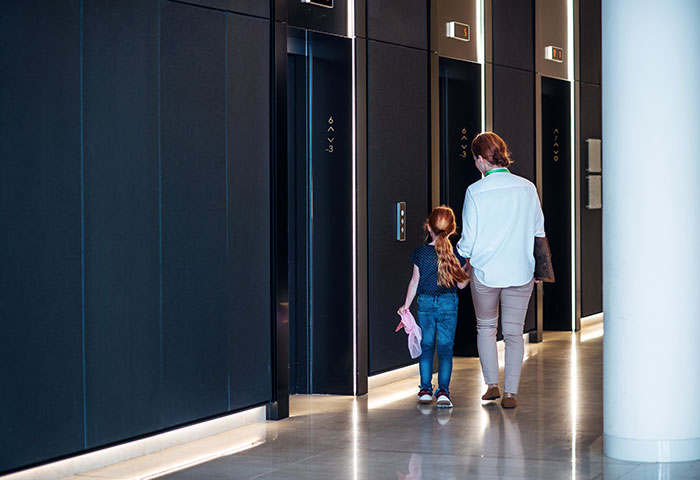 Parent and child walking toward elevators in a modern hallway, capturing embarrassing moments parents will never forget.