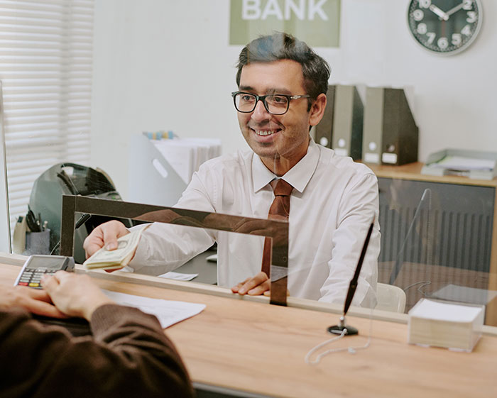 Bank teller smiling and handing cash to a customer, illustrating an everyday moment parents will never forget.