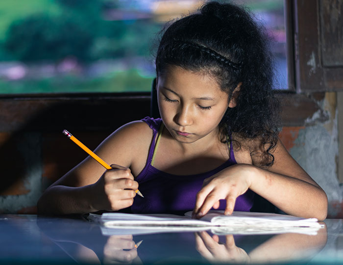 Young girl with curly hair focused on writing in a notebook, illustrating embarrassing moments parents experience with kids.