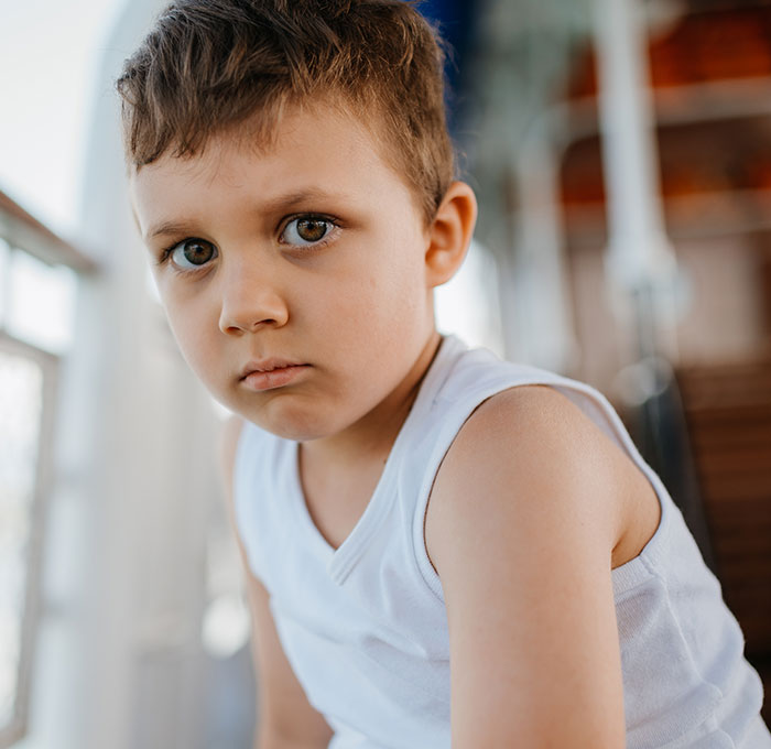 Close-up of a serious young boy in a white tank top, capturing a candid moment parents will never forget thanks to their kids.
