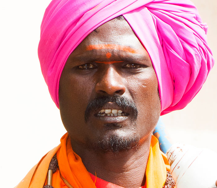 Close-up of a man with dark skin wearing a bright pink turban and orange clothing, highlighting black skin features.