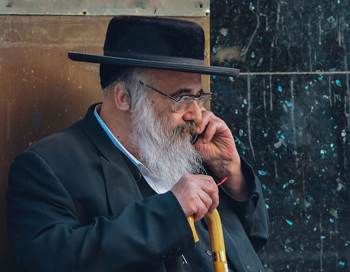 Elderly man with a beard and hat holding a cane and talking on a phone, reflecting on embarrassing moments parents face.