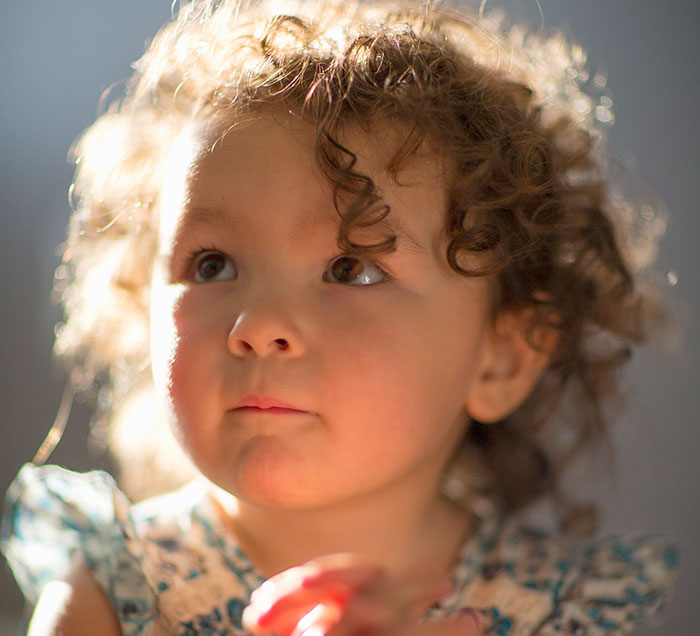 Close-up of a toddler with curly hair in soft natural light, capturing an innocent and thoughtful expression from the child.