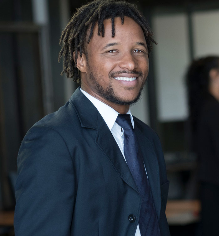 Smiling man with dreadlocks wearing a dark suit and tie, representing black parents in memorable embarrassing moments with kids.