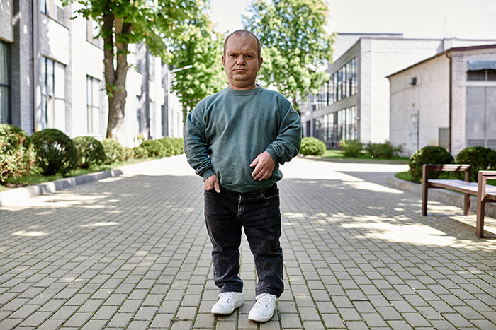 Man with dwarfism standing outdoors between buildings on a sunny day, illustrating embarrassing moments parents will never forget.