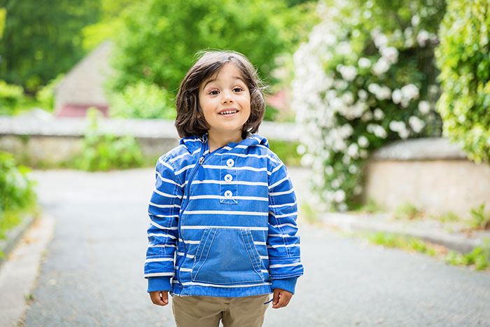 Child in a blue striped hoodie smiling outdoors, capturing embarrassing moments parents will never forget thanks to kids.
