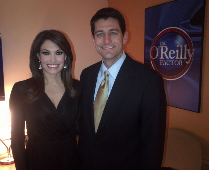 Kimberly Guilfoyle and a man posing indoors with the O'Reilly Factor poster visible in the background.