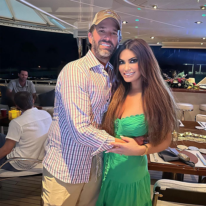 Kimberly Guilfoyle posing with Donald Trump jr. on a yacht at night, showcasing her style in a green dress with long hair.